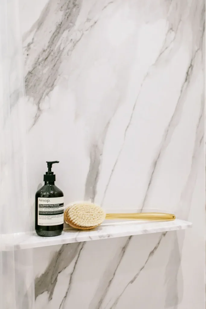 Chic bathroom shelf styled by Rebel Arkitekt, displaying high-end personal care products against a luxurious marble backdrop, embodying the apartment's blend of functional design with a touch of opulence.