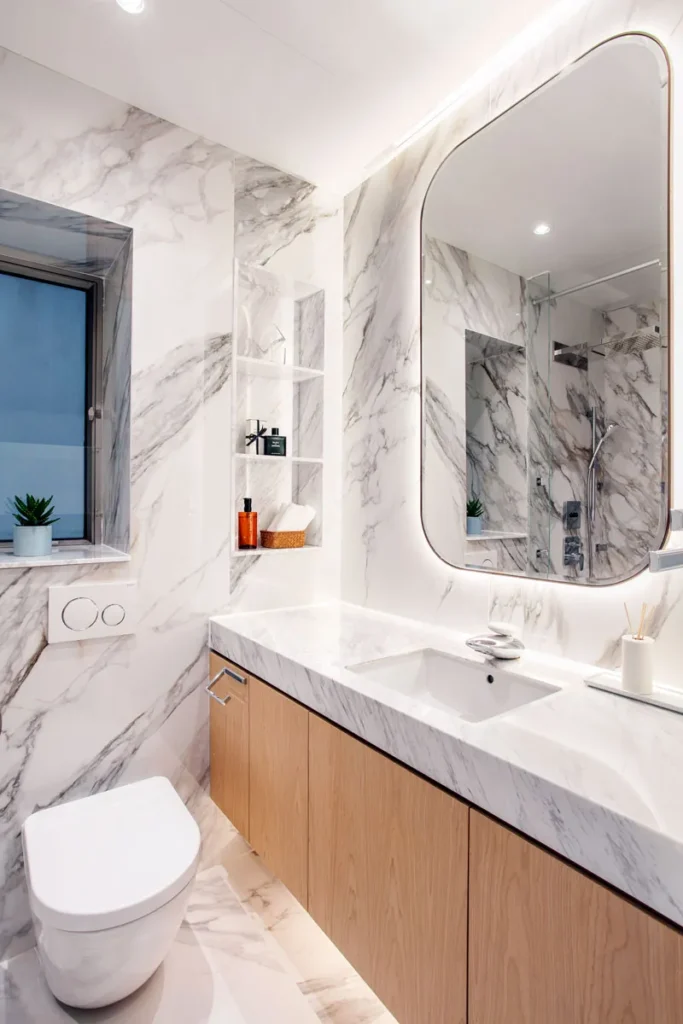 Sophisticated guest bathroom featuring marble walls and countertop with an arched mirror, designed by Rebel Arkitekt to create a seamless blend of luxury and minimalism.