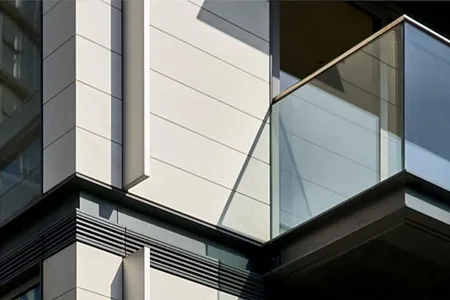 Architectural detail of a waterfront apartment facade, highlighting the interplay of shadow and light on its white paneling, clean lines, and transparent glass balcony, reflecting a clear blue sky.