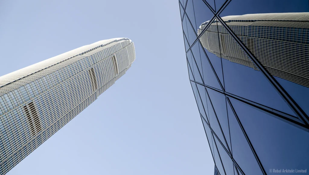 Reflective skyscraper façade capturing the mirror image of its towering neighbor against a clear blue sky, a visual narrative by Rebel-i from Rebel Arkitekt.