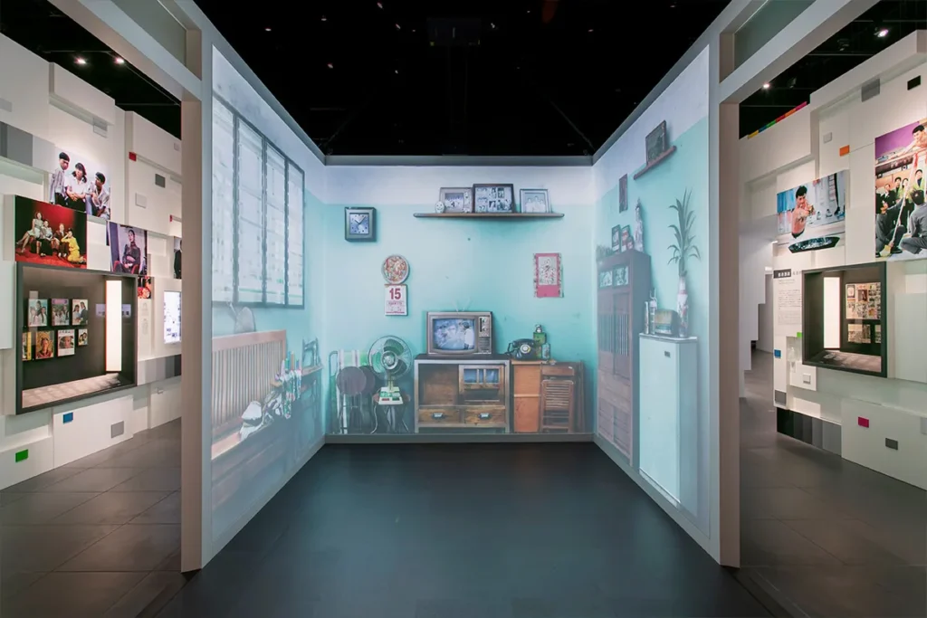 A spacious exhibit area seamlessly merges a nostalgic video room installation with a contemporary gallery, featuring a light blue wall that gives the illusion of an intimate living space, all under the project management of Rebel Akitekt.