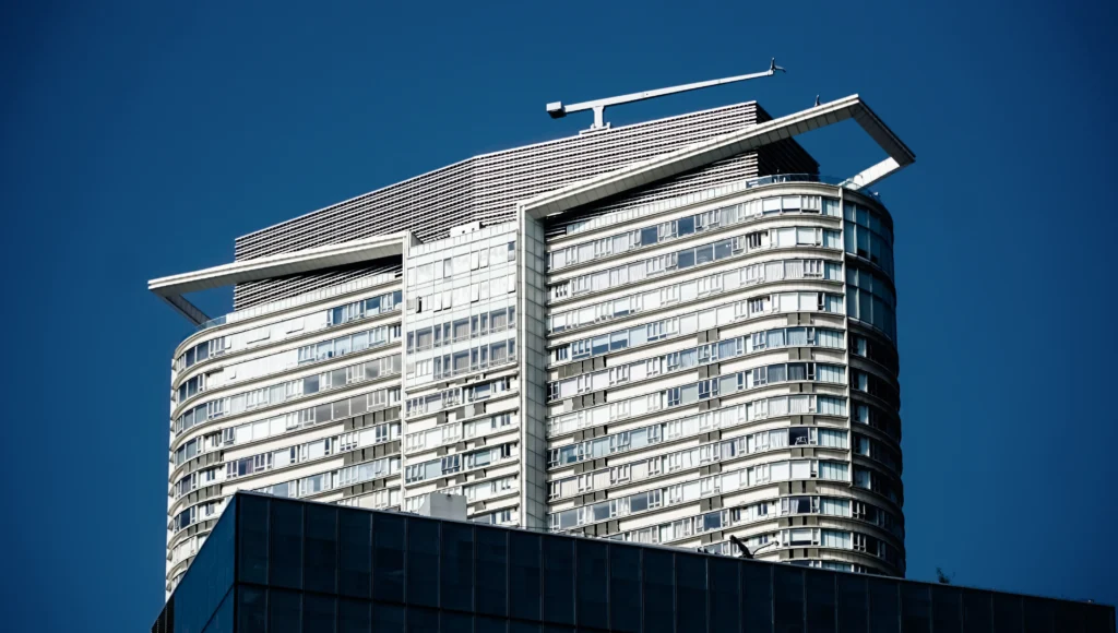 Modern skyscraper with a distinctive crown-like structure atop, set against a clear sky in a photograph by Rebel-i from Rebel Arkitekt.