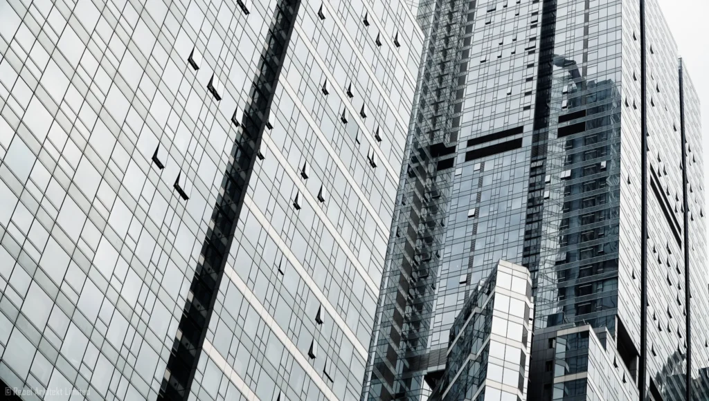 an angled view of a modern skyscraper's facade with a dynamic interplay of glass windows and geometric lines against a clear sky, captured by Rebel Arkitekt, emphasizing the sleek design and towering presence of contemporary urban architecture.