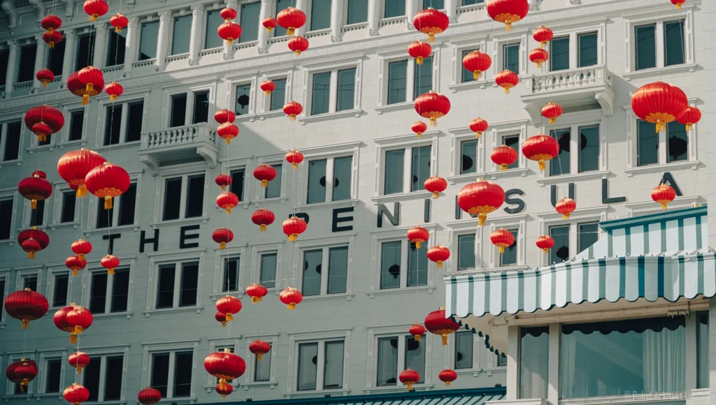 Vibrant red Chinese lanterns float against a classical white facade of The Peninsula, illustrating the elegant blend of Eastern and Western influences, captured by Rebel Arkitekt, highlighting cultural fusion in architectural spaces.