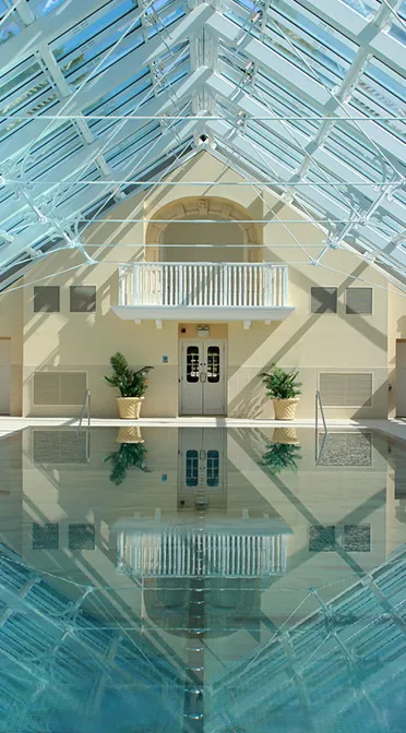 Symmetrical view of an indoor pool with a vaulted glass ceiling and serene water.