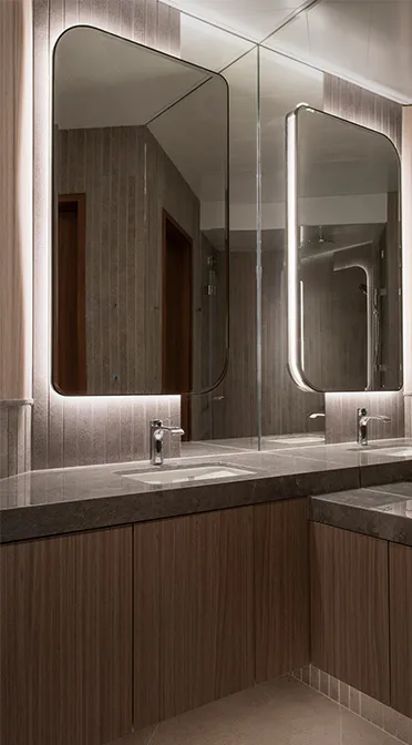 Sophisticated bathroom detailing by Rebel Arkitekt, with rich wood grain cabinetry and a sleek countertop surrounding an under-mount sink, complemented by a custom mirror with integrated lighting, capturing a refined elegance.