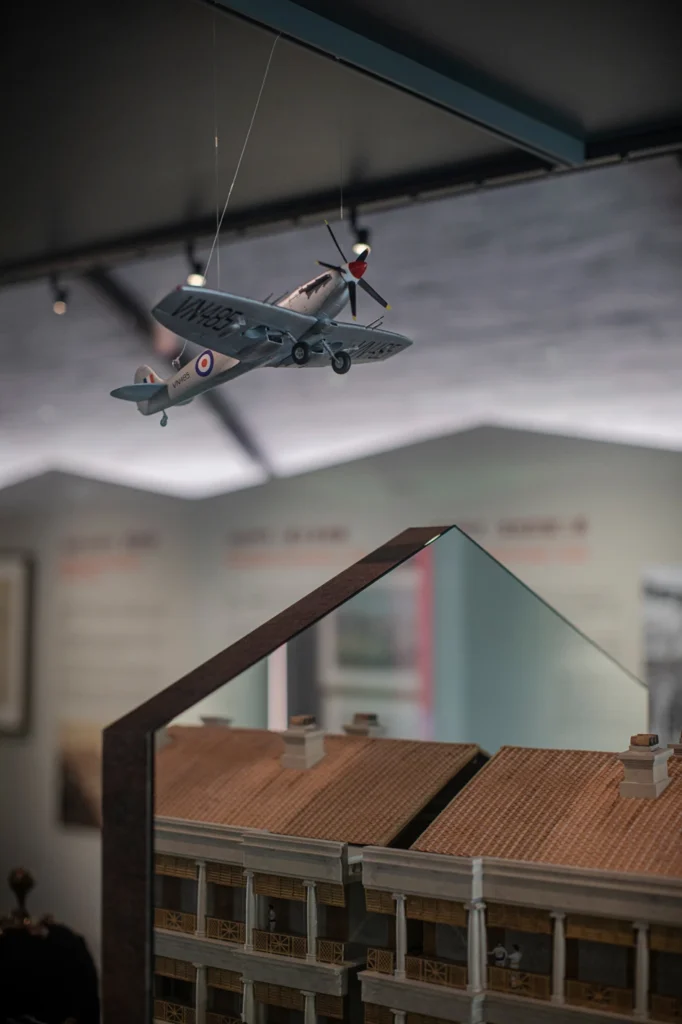 Model of a historic aircraft suspended above a detailed replica of colonial-style buildings at the Hong Kong Museum of Coastal Defence.