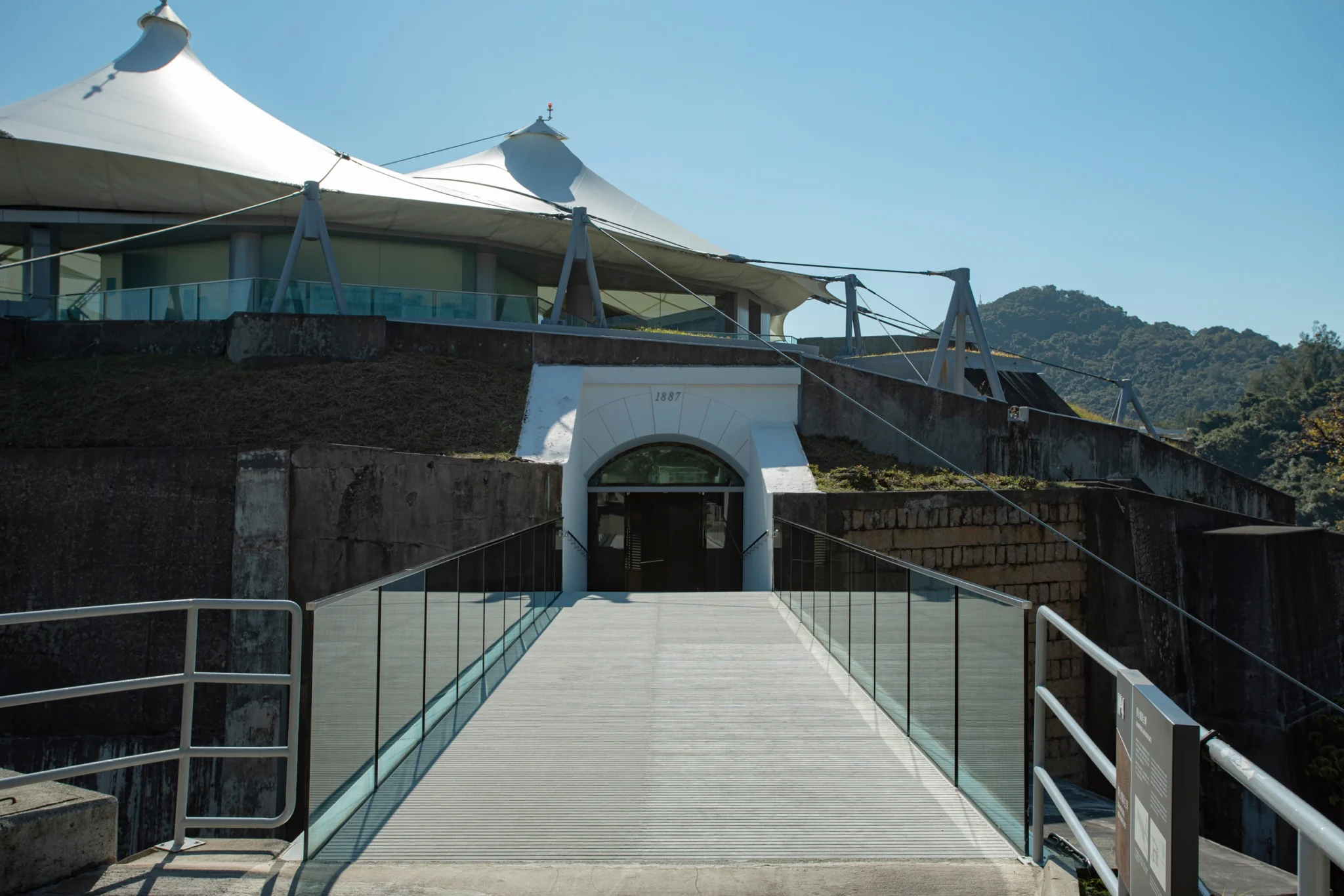 The 1887 fort entrance, now part of the HK Museum of Coastal Defence, features preserved stonework enhanced by a modern glass bridge.