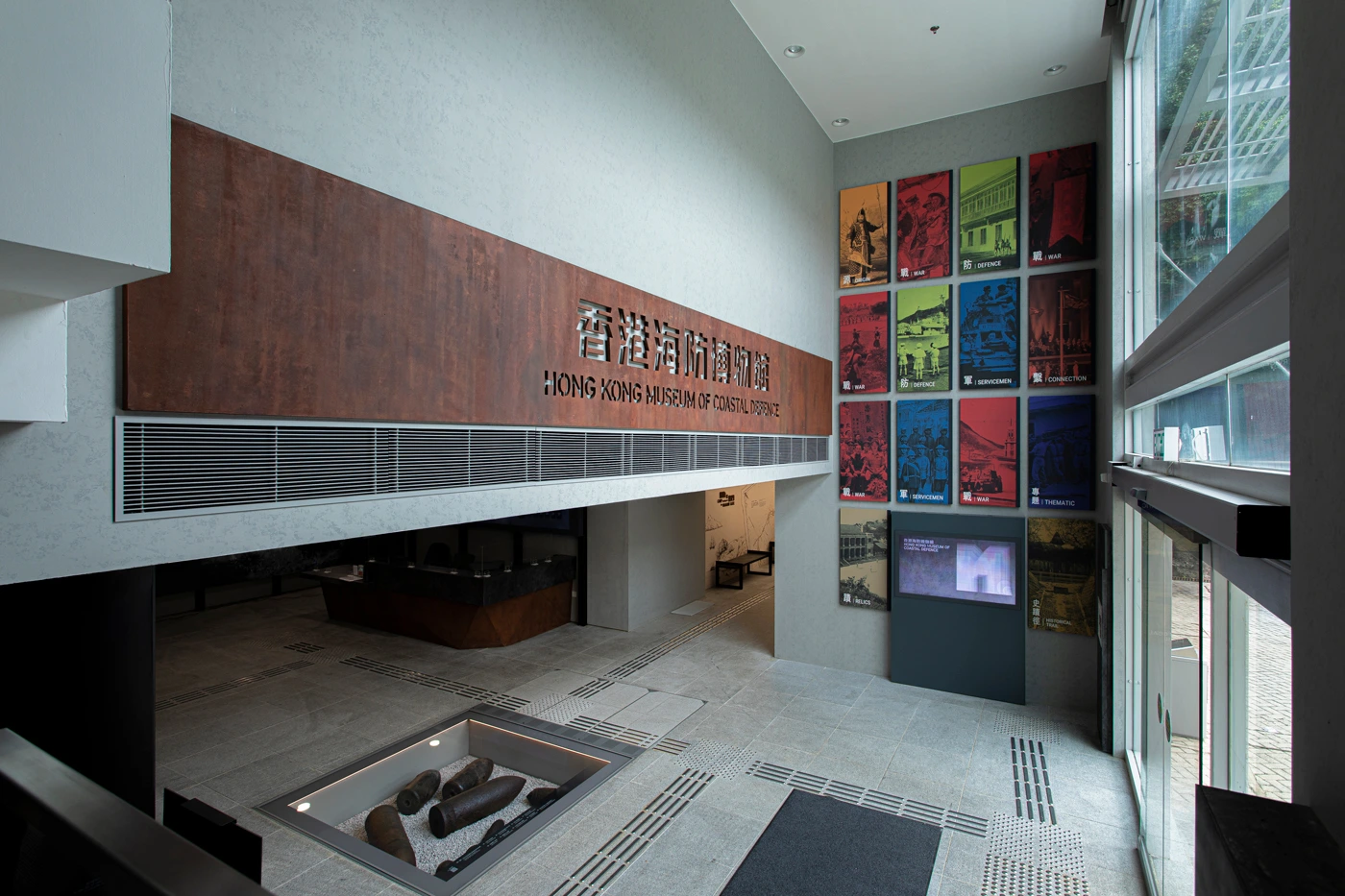 Main entrance of the Hong Kong Museum of Coastal Defence, showcasing a rust-textured sign and colorful wall panels depicting themes of war and defence