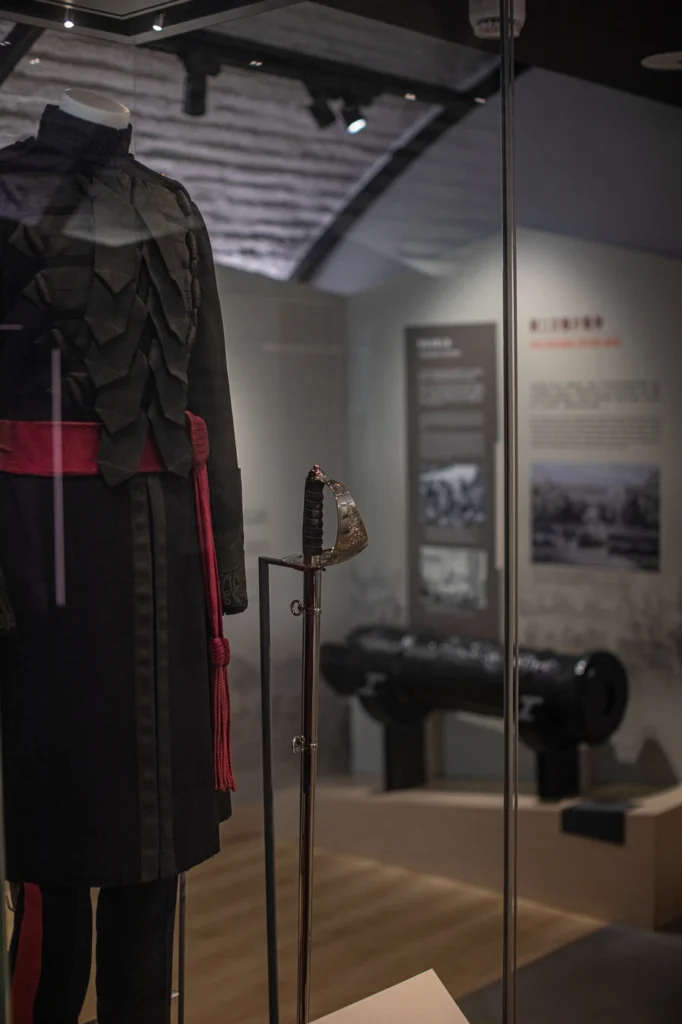 Elegant military uniform and sword display narrating Hong Kong’s martial history, set against a backdrop of historical cannons and informational panels