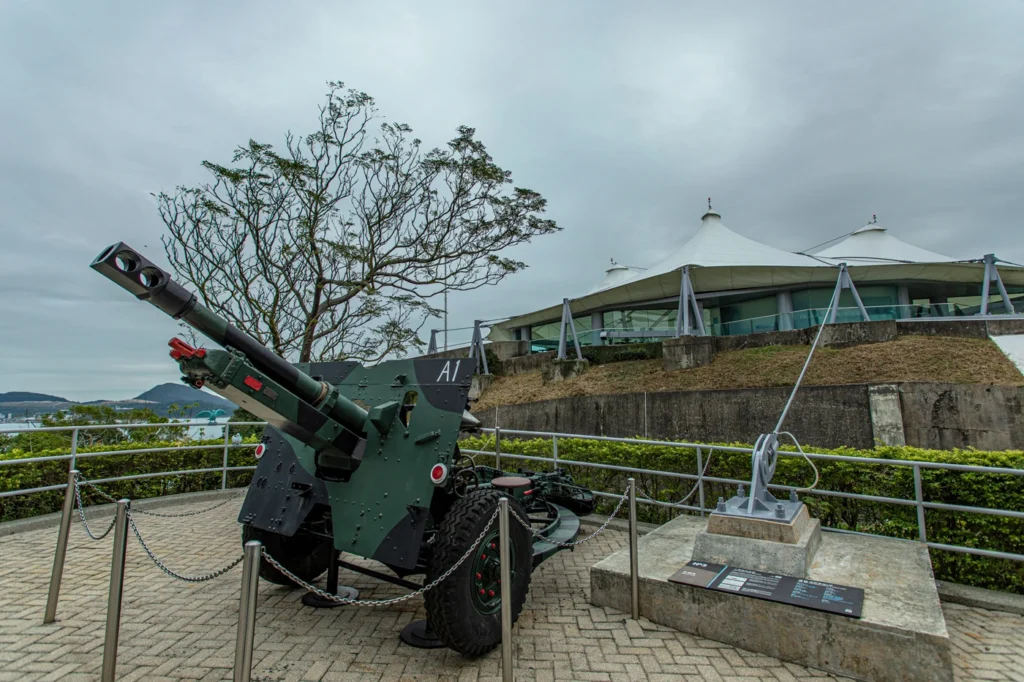 Outdoor artillery display featuring a green field gun and an anchor sculpture at the Hong Kong Museum of Coastal Defence.