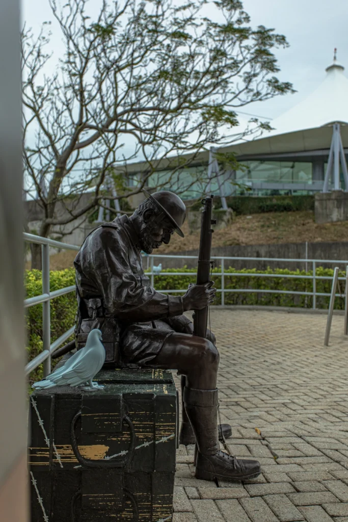 Bronze statue of a soldier seated with a rifle, accompanied by a symbolic dove, at the Hong Kong Museum of Coastal Defence.